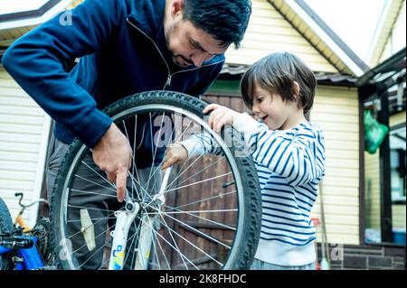 Sohn hilft Vater Reparatur Fahrrad Rad vor Haus Stockfoto