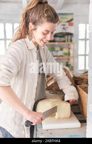 Lächelnder Lebensmittelhändler, der Käse im Lebensmittelgeschäft schneidet Stockfoto