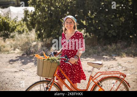 Lächelnde ältere Frau mit Gemüse im Fahrradkorb Stockfoto