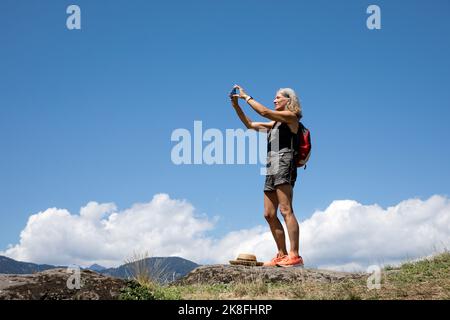 Ältere Frau, die an einem sonnigen Tag per Smartphone fotografiert Stockfoto