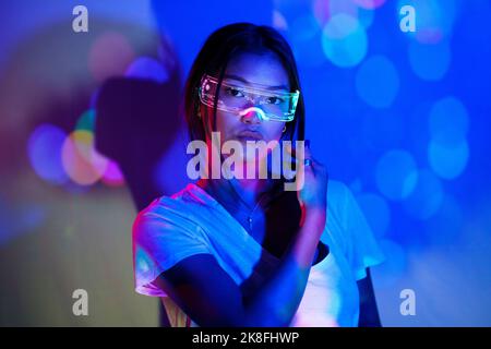 Selbstbewusste junge Frau mit einer smarten Brille vor der Wand Stockfoto