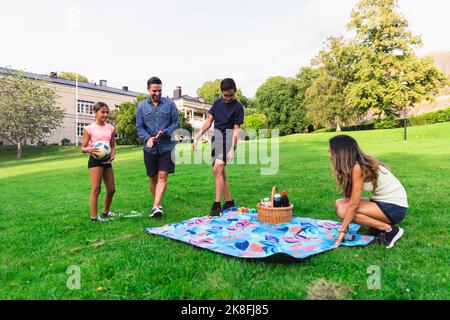 Frau legt Picknickdecke mit Familie auf Gras im Rasen Stockfoto