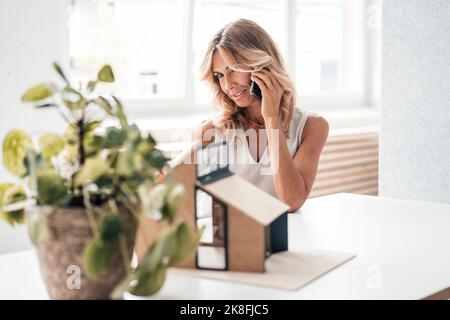 Architekt im Gespräch über Smartphone mit Blick auf das Hausmodell im Büro Stockfoto