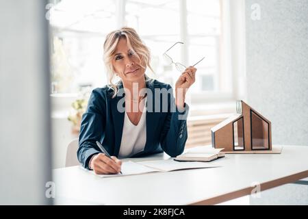 Immobilienmakler hält Brillen am Schreibtisch im Büro Stockfoto