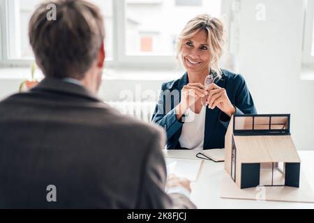 Lächelnder Immobilienmakler, der den Kunden im Büro ansieht Stockfoto