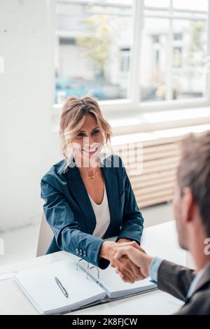 Lächelnde Geschäftsfrau schüttelt sich die Hände mit dem Mann im Büro Stockfoto