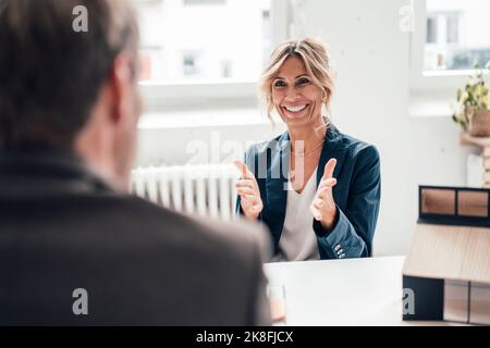 Aufgeregter Immobilienmakler, der im Büro gestikuliert und mit dem Kunden gesprochen hat Stockfoto