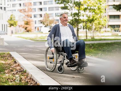 Lächelnder älterer Mann im Pullover, der auf dem Rollstuhl sitzt Stockfoto
