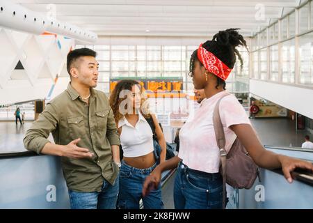 Multirassische junge Männer und Frauen, die auf der Rolltreppe am Bahnhof sprechen Stockfoto