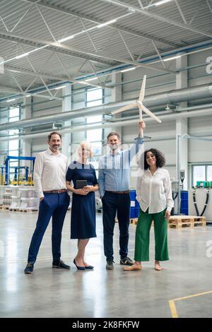 Ein reifer Geschäftsmann, der ein Windenergieanlagenmodell hält, das von Kollegen in der Industrie steht Stockfoto