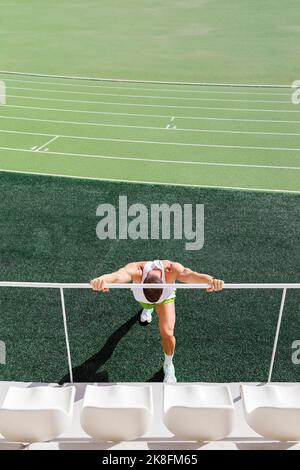 Athlet macht warme Übungen durch Geländer auf dem Sportplatz Stockfoto