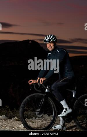 Lächelnder Radfahrer mit Helm und Fahrrad in der Abenddämmerung Stockfoto