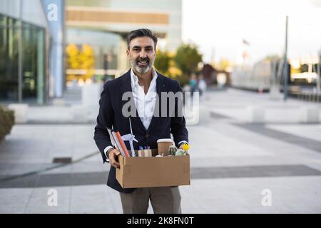 Lächelnder Geschäftsmann hält einen Kasten mit Büromaterial Stockfoto