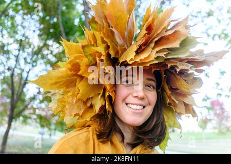 Lächelnde Frau mit Kranz aus Herbstblättern im Park Stockfoto