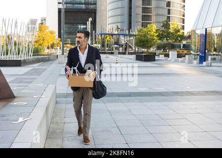 Ein Geschäftsmann hält einen Kasten in der Hand, der vor dem Bürogebäude läuft Stockfoto