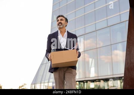 Lächelnder Geschäftsmann verlässt das Büro mit Büromaterial in einem Karton Stockfoto