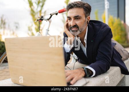 Geschäftsmann mit Kopfhörern und einem Laptop auf der Bank Stockfoto