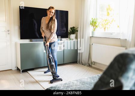 Lächelnde Frau, die zu Hause den Staubsauger auf dem Teppich verwendet Stockfoto