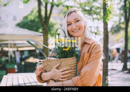 Lächelnde Frau mit Blumen in Weidensack auf dem Markt Stockfoto