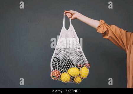 Frau mit Zitronen und Gemüse in einem Netzbeutel vor grauem Hintergrund Stockfoto