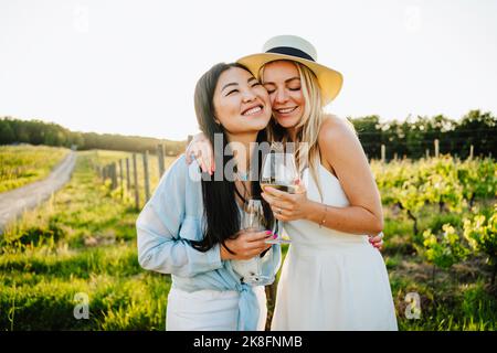 Glückliche Freunde halten ein Glas Wein umarmt in der Weinkellerei Stockfoto