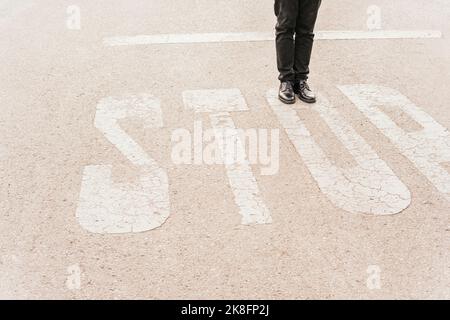 Die Beine des Mannes auf DEM STOPPSCHILD an der Straße Stockfoto