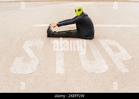 Mann mit Alien-Maske sitzt vor dem STOPPSCHILD auf der Straße Stockfoto