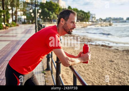 Lächelnder Mann, der die Wasserflasche am Geländer hält Stockfoto