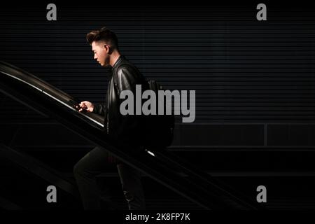 Mann, der Smartphone auf der Rolltreppe benutzt Stockfoto