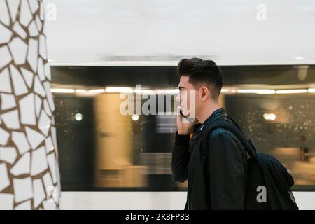 Junger Mann, der am Bahnhof mit dem Handy telefoniert Stockfoto