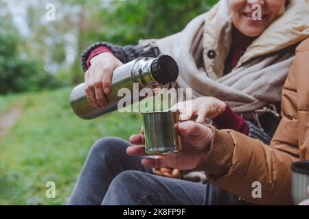 Frau, die Wasser aus Thermoskannen von einem Mann im Wald gießt Stockfoto