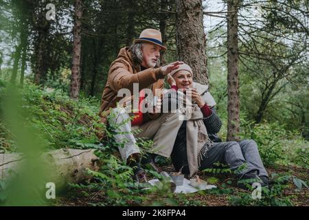 Glückliches Paar, das auf Baumstamm im Wald sitzt und redet Stockfoto