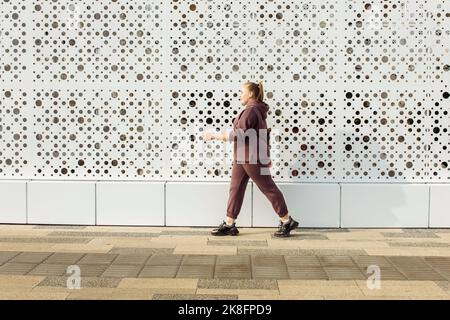 Übergewichtige Frau im Kapuzenhemd, die an der Wand entlang läuft Stockfoto