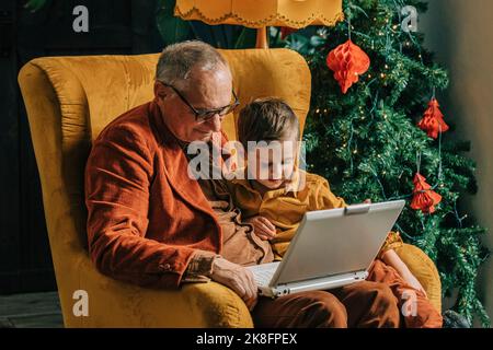 Großvater und Junge sitzen im Sessel mit Laptop von Weihnachtsbaum Stockfoto