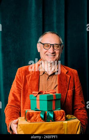 Glücklicher älterer Mann, der mit Geschenkschachteln vor dem Vorhang steht Stockfoto