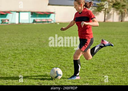 Mädchen tritt Fußball auf dem Feld an sonnigen Tag Stockfoto