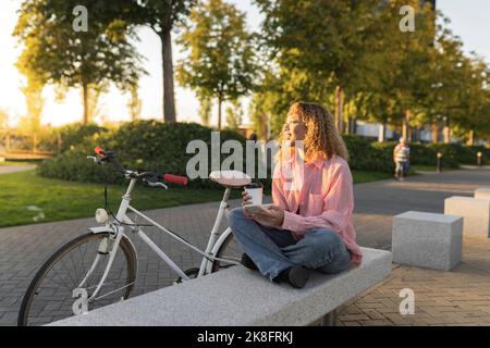 Nachdenkliche Frau mit Einweg-Kaffeetasse auf der Bank sitzen Stockfoto