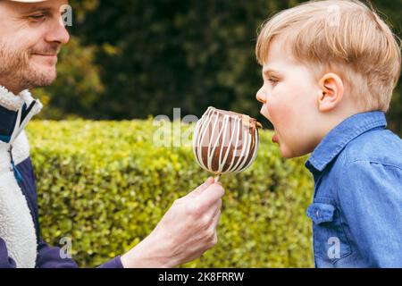 Lächelnder Vater füttert im Park einen pfeifigen Apfel an den Sohn Stockfoto