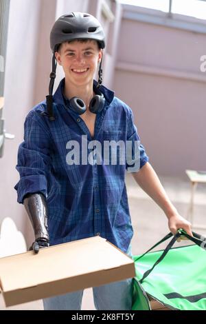 Lächelnder Teenager mit einem amputierten Arm, der eine Pizzabox hält Stockfoto