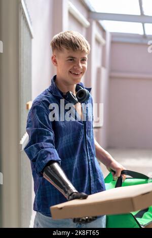 Lächelnder Teenager mit einem prothetischen Arm, der eine Pizzabox hält Stockfoto