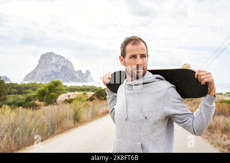 Nachdenklicher Mann mit Haarstoppel, der Skateboard trägt Stockfoto