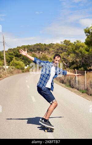 Mann mit ausgestreckten Armen Skateboarding an sonnigen Tag Stockfoto