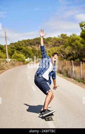 Mann mit erhobener Hand genießt Skateboarding an sonnigen Tagen Stockfoto