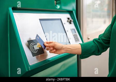 Hand einer Frau, die an der Straßenbahnhaltestelle die Kreditkarte auf den Ticketautomaten klopft Stockfoto