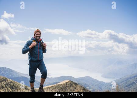 Glücklicher reifer Mann mit Strickmütze, der vor dem wolkigen Himmel steht Stockfoto