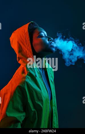 Hipster Frau im Regenmantel weht Rauch aus dem Mund Stockfoto