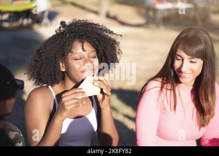 Multiethnische Freundinnen genießen ein gemeinsames Picknick im Freien in einem Park. Freundschaftskonzept. Stockfoto