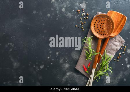 Kochgeschirr aus Holz, Basilikumblätter und Gewürze auf altem Holzhintergrund. Abstrakter Lebensmittelhintergrund. Draufsicht auf dunklen rustikalen Küchentisch mit Holz Stockfoto