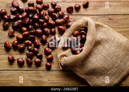 Blick von oben auf frische Kastanien im Sack auf alten Holztisch Stockfoto