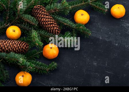 Weihnachtlicher Hintergrund mit Mandarinen, Tannenzweigen, Zapfen auf schwarzem Tisch. Draufsicht, Kopierbereich Stockfoto